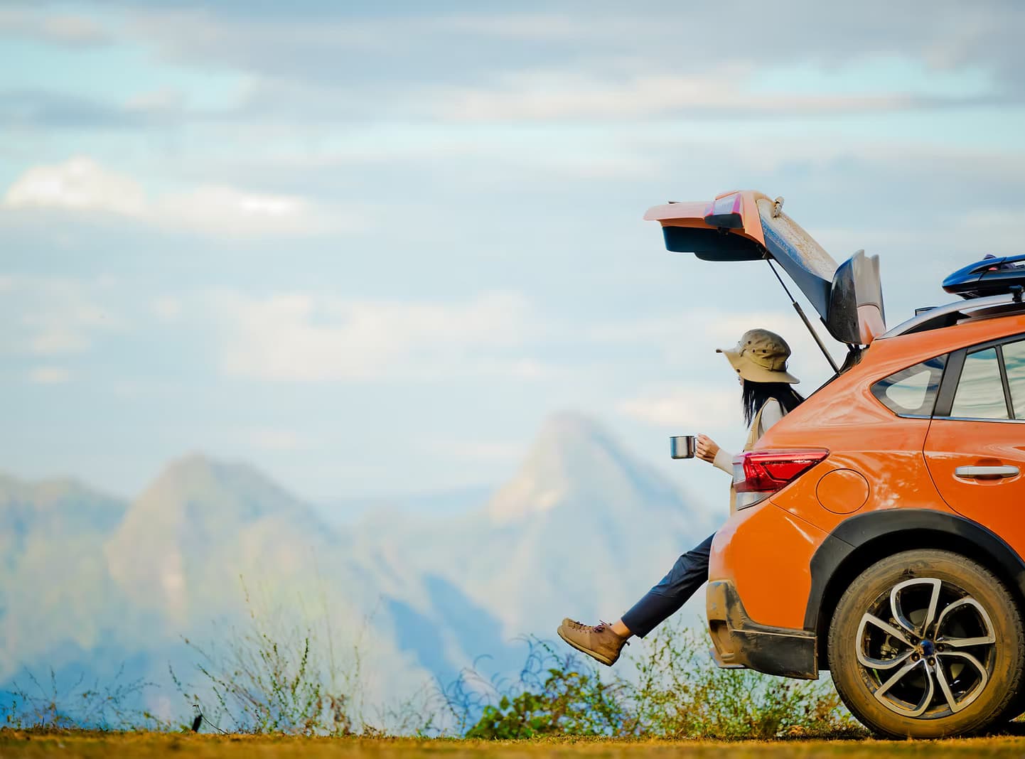 A person sitting on the back of their car, looking at mountains